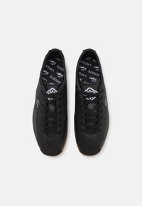 Baskets noires avec une tige en cuir texturé, bout rond, design à lacets et semelle en caoutchouc gomme. Présente un intérieur noir avec logo.