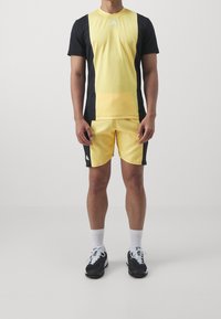 Żółty i czarny strój sportowy składający się z koszulki z krótkim rękawem z fakturowanym przodem i pasujących szortów. Znaleziony w połączeniu z czarnymi butami sportowymi i białymi skarpetkami.