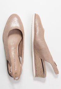 Beige sleehakken met een bovenwerk van suede, open zijkanten en een glanzende afwerking. Kenmerkt zich door een gestructureerde gevlochten accent op de hak en een gevoerde binnenzool.