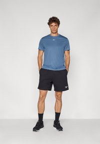 Modrá športová tričko s krátkymi rukávmi a okrúhlym výstrihom, skombinované s čiernymi šortkami. Čierne tenisky a ponožky dotvárajú look.