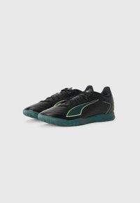 Par de zapatillas deportivas negras de corte bajo con suelas verdes y acentos de logo verdes, mostradas en un ligero ángulo sobre fondo blanco.