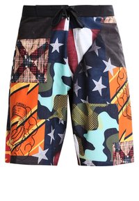 Färgglada badshorts med olika överlappande mönster, inklusive stjärnor, rutigt och camouflage, med dragsko i midjan och lätt tyg.