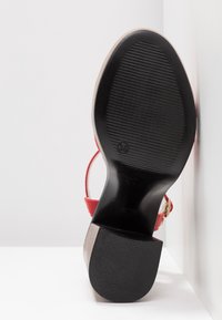 Semelle d'une chaussure à talon haut rouge avec semelle noire texturée antidérapante, talon empilé et indication de taille 38 visible.