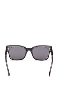 Ochelari de soare de formă pătrată, cu lentile gri închis, rame negre transparente, accente aurii pe balamale și brațe negre elegante.