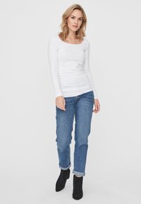 Witte lange mouwen top met een ronde hals, gecombineerd met blauwe opgerolde jeans en zwarte enkellaarsjes. De stof lijkt glad en aansluitend.