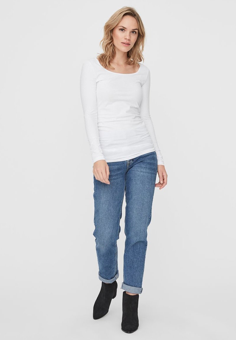 Witte lange mouwen top met een ronde hals, gecombineerd met blauwe opgerolde jeans en zwarte enkellaarsjes. De stof lijkt glad en aansluitend.