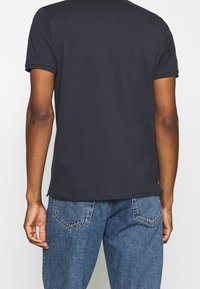 T-shirt bleu marine à manches courtes avec col rond, fabriqué en coton, présentant un ourlet droit et des fentes latérales discrètes. Assorti à un jean en denim bleu.