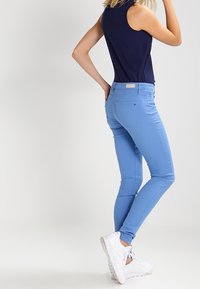 Jeans ajustados de color azul cielo, confeccionados con una mezcla de algodón, que presentan una cintura de altura media, bolsillos traseros y una textura suave y elástica.
