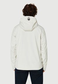 Vit huvad jacka med en slät textur, med en svart logodetalj på ryggen och en figursydd passform, matchad med mörka byxor.