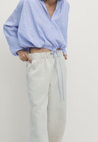 Chemise en lin bleu clair, ample, au design court avec détails à boutons, associée à un pantalon large couleur crème avec taille élastique.