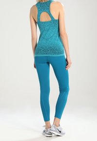 Camiseta deportiva sin mangas color verde azulado con diseño de espalda abierta, combinada con leggings del mismo color. Presenta texturas suaves y un estilo ajustado.