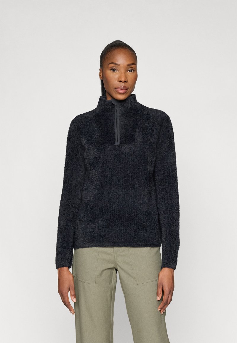 Sort fleece-pullover med høj krave og halv-lynlås foran. Blødt, struktureret materiale med lange ærmer, parret med olivengrønne bukser.
