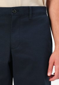 Sötétkék pamut nadrág sima textúrával, elülső zsebbel, övhurkokkal és gombos záródással a derékon.