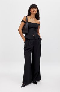 Čierny off-shoulder peplum top s detailom gombíka, skombinovaný s čiernymi nohavicami s vysokým pásom a širokými nohavicami a čiernymi špicatými topánkami.