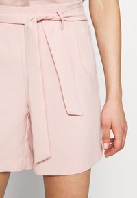Shorts en tissu rose à texture lisse, avec une ceinture nouée à la taille et une coupe décontractée. Pas de motifs ni de garnitures visibles.