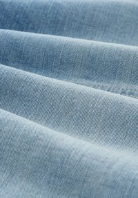 Svijetloplava denim tkanina s glatkom teksturom, koja sadrži dijagonalne satenaste uzorke i suptilne vertikalne pruge, raspoređene u blagim naborima.