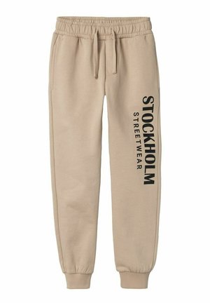 Pantalones jogger beige con cintura y puños elásticos, cordón en la cintura y la inscripción "STOCKHOLM STREETWEAR" impresa verticalmente en la pierna izquierda.
