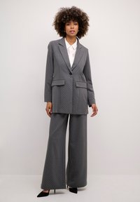 Pelēku punktiņu kostīms, kas ietver pielāgotu bleizeri ar iecirtīgām kabatām un platām biksēm. Valkāts virs baltas krekls, apvienots ar melniem papēžiem.