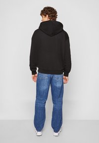 Sudadera con capucha negra de algodón con un corte relajado, combinada con pantalones vaqueros azul denim de corte clásico y detalles de costura visibles.