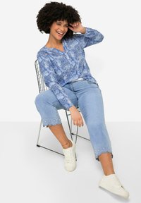 Blusa azul con estampado, de mangas largas y corte holgado. Jeans cortos de color azul claro con un dobladillo con forma de ondas. Zapatillas blancas completan el atuendo.