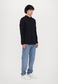 Zwarte langarm button-up shirt van lichtgewicht stof, gecombineerd met lichtblauwe jeans en witte sneakers. Eenvoudig ontwerp, ontspannen pasvorm.