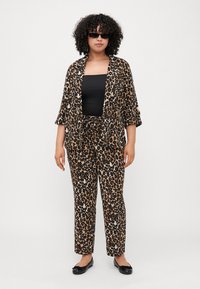 Leopardenmuster Zweisitzer-Outfit mit einer lässigen, offenen Jacke und passenden Hosen. Der Stoff ist leicht und hat eine glatte Textur. Schwarze Ballerinas sind enthalten.