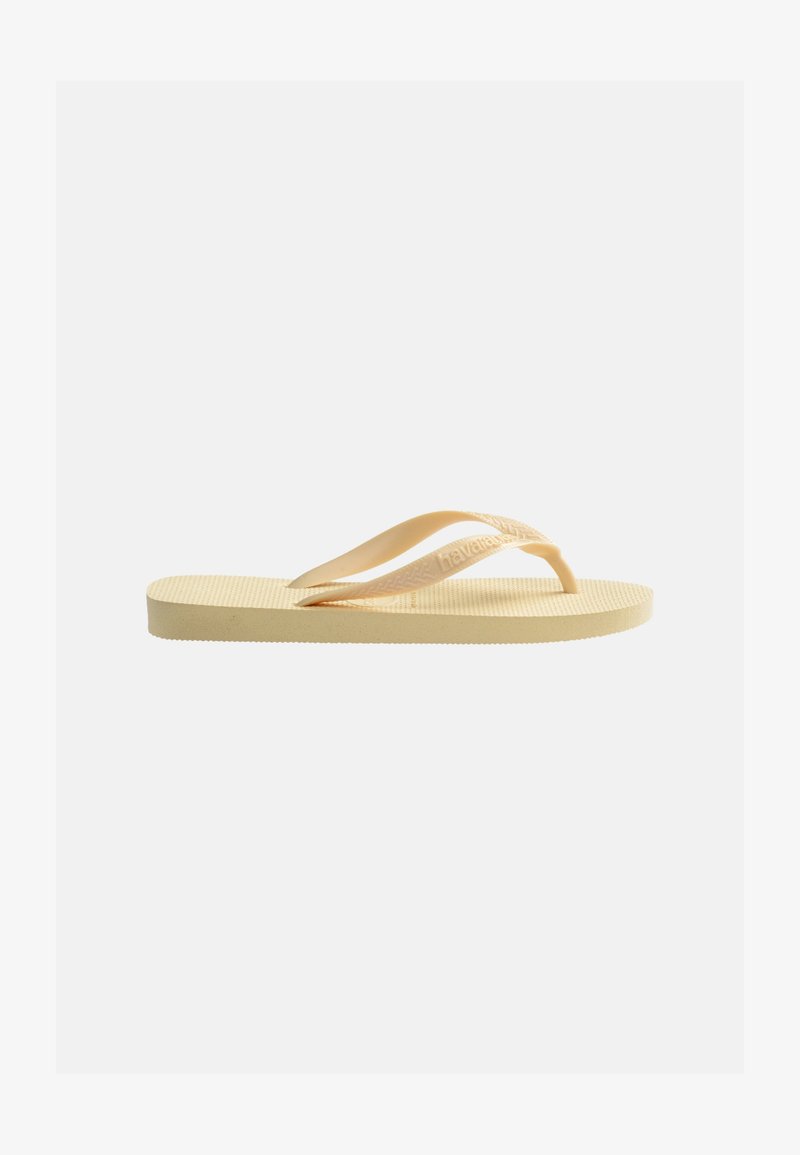 Μπεζ λαστιχένια σαγιονάρα με υφή στη σόλα και λουριά σε σχήμα Υ, τοποθετημένη στο πλάι πάνω σε απλό ανοιχτό φόντο.