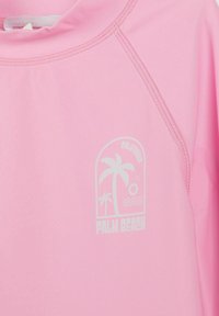 Roosa särk valge trükitud pildiga palmipuudest, päikesest, lainetest ja tekstist "California Palm Beach" rinnapiirkonnas.