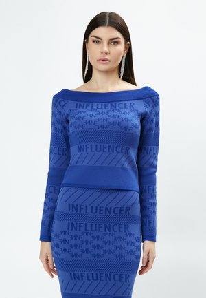 Blauwe gebreide jurk met lange mouwen, off-shoulder ontwerp en een herhalend tekstpatroon van "INFLUENCER". De textuur varieert met strepen en stippen.