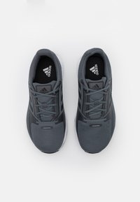 Šedé sportovní boty s síťovinovým materiálem, zavazováním na tkaničky a bílou podrážkou; mají po stranách tři černé pruhy a polstrovaný límec.