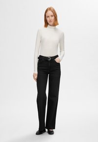 Bela dolgim rokavom turtleneck majica v kombinaciji z visokim pasom črnimi kavbojkami. Obleka ima pas s srebrno sponko in ravne črne čevlje.