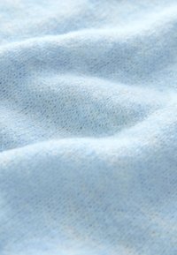 Mīksta, gaiši zila adīta auduma ar pūkainu tekstūru un smalkām krokām, kas rada maigas viļņošanās pa virsmu.