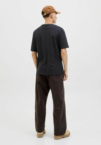 Dunkelgraues Baumwoll-T-Shirt mit einem lässigen Schnitt, kombiniert mit dunkelbraunen Cargo-Hosen und beigen Stiefeln, von hinten betrachtet. Eine braune Mütze hebt das Outfit hervor.