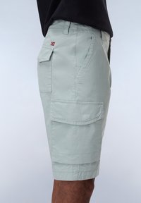 Pantaloni cargo verde chiaro con multiple tasche, dettagli cuciti e un piccolo emblema a forma di bandiera sul lato. Realizzati in cotone, design fino al ginocchio.