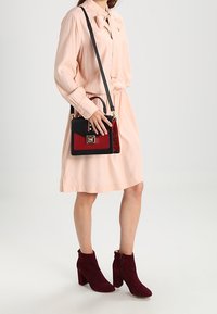 Růžová dlouhá šatová šaty s lněným límcem, doplněná o tmavě červené kotníkové boty a malou černou a červenou kabelku.