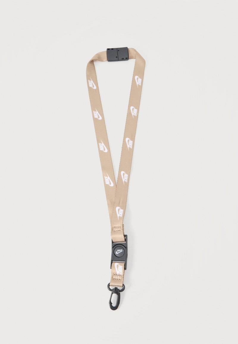 Béžový šnúrka Nike s bielymi logami, čiernou plastovou sponou a kovovým háčikom na pripevnenie kľúčov alebo preukazov totožnosti.