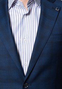 Granatowa marynarka w kratę z wyraźnymi klapami, zestawiona z jasnoniebieską koszulą w białe paski z zapięciem na guziki przy kołnierzyku i mankietach.