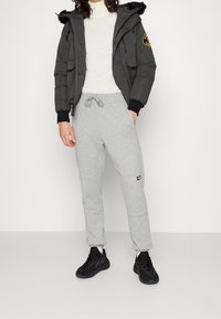 Grå sweatpants med elastisk talje og snøre, parret med en sort puffjakke med et logo-patch og sorte sportsko.