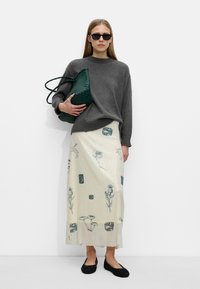 Szary sweter z dzianiny, kremowa spódnica w kwiatowy wzór, zielona pleciona torebka oraz czarne buty wsuwane. Ubranie charakteryzuje się różnorodnymi teksturami i kolorami.