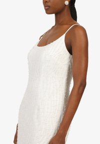 Weißes Perlenkleid mit taillierter Silhouette, dünnen Trägern und einem strukturierten Muster, das durch vertikale Reihen von Perlen entsteht.