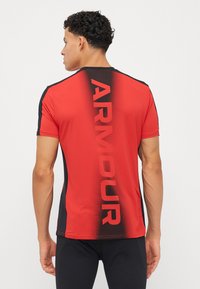 Rød og svart kortermet treningsskjorte med "ARMOUR" trykket vertikalt på ryggen. Glatt tekstur, tettsittende design, kontrasterende sidepaneler.