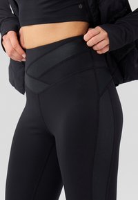 Sorte høy midje leggings laget av elastisk stoff med en glatt overflate, med paneldesign og forsterket søm langs sømmene.