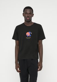 Fekete pamut póló grafikával, melyen absztrakt kék és narancs formák, valamint "MATISSE" felirat látható. Kerek nyakkivágású, rövid ujjú.