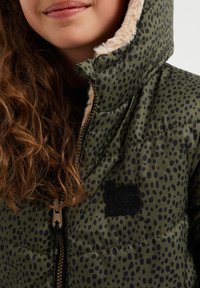 Grön puffjacka med svarta prickar, utrustad med huva foder i konstpäls och dragkedjestängning, accentuerad av en svart tyglogotyp.