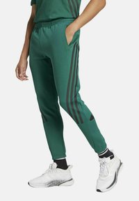 Pantaloni sportivi verdi realizzati in tessuto leggero, con strisce laterali nere, vita elastica e tasche laterali per maggiore comodità.