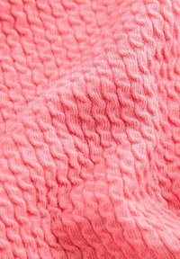 Texturerad rosa tyg med ett vågmönster, tillverkat av mjukt garn. Ytan ser lyxig och något fuzzy ut, vilket framhäver djup och detalj.