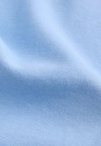 Svijetloplavi, fino teksturirani materijal s diskretnim rebrastim uzorkom, mekan na dodir, lagano se spušta u glatke valove.