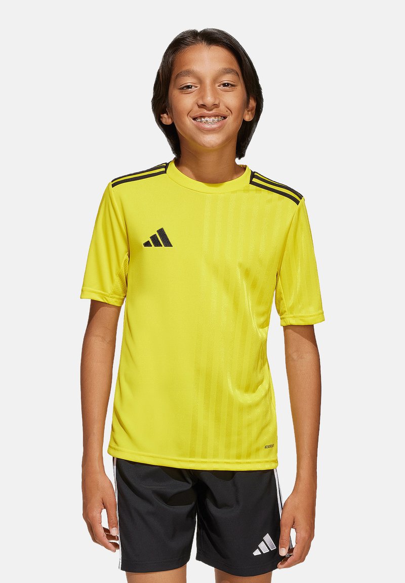 Geel Adidas voetbalshirt met korte mouwen, zwarte drie-streepdashouderaccenten en een verticale streepstructuur. G gedragen met zwarte shorts.