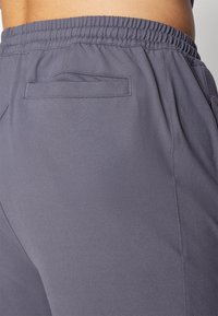 Grijze sportbroek met een elastische tailleband, voorzien van een achterzak en een gladde stofstructuur. Eenvoudig ontwerp, gericht op comfort.
