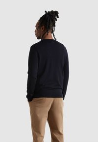 Navy-blau gestrickter Pullover mit Rundhalsausschnitt und langen Ärmeln, kombiniert mit hellbraunen Hosen; glatte Textur, enganliegendes Design.